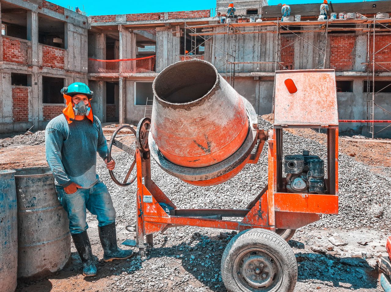 A construction worker operating a concrete mixer at an active building site, emphasizing safety gear.